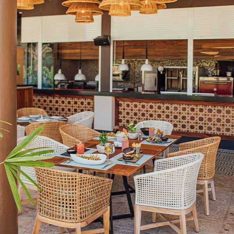 Comedor del restaurante On the Waves en Jungala Aqua Experience, con mesas de madera y sillas de mimbre
