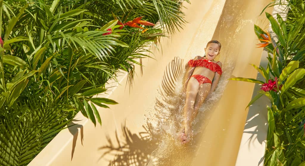 Niña deslizándose por un tobogán infantil en Jungala Aqua Experience, rodeada de vegetación tropical