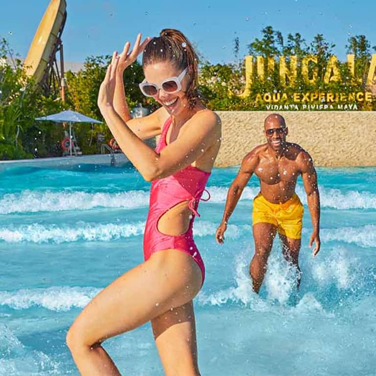 Pareja divirtiéndose en la alberca de olas de Jungala Aqua Experience con el letrero del parque de fondo