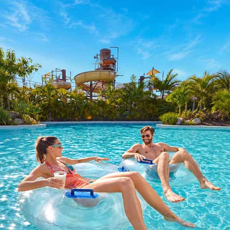 Pareja en donas inflables en el río lento de Jungala Aqua Experience con la torre de toboganes de fondo