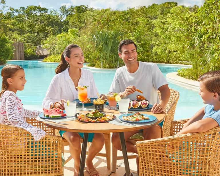 Familia disfrutando de una comida en On the Waves, con vista a la alberca en Jungala Aqua Experience