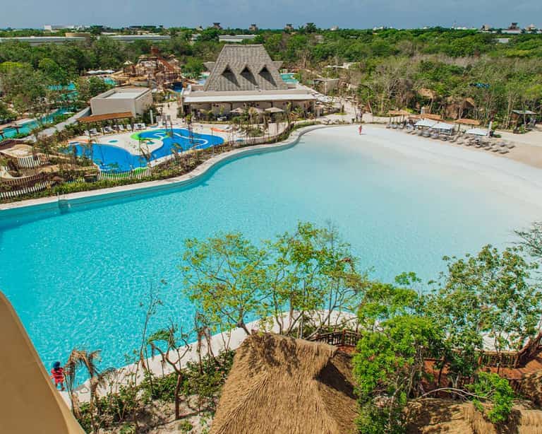 Vista aérea de la alberca de olas en Jungala Aqua Experience, con entrada de arena y palapa de fondo