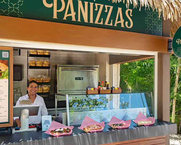 Empleada atendiendo el mostrador de Panizzas con pizzas en exhibición en Jungala Aqua Experience