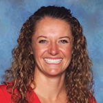 A person with curly hair wearing a red top in front of a blue background.