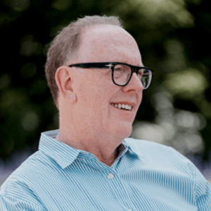 Person wearing glasses and a light blue striped shirt outdoors with a blurred background. Person wearing glasses and a light blue striped shirt outdoors with a blurred background.