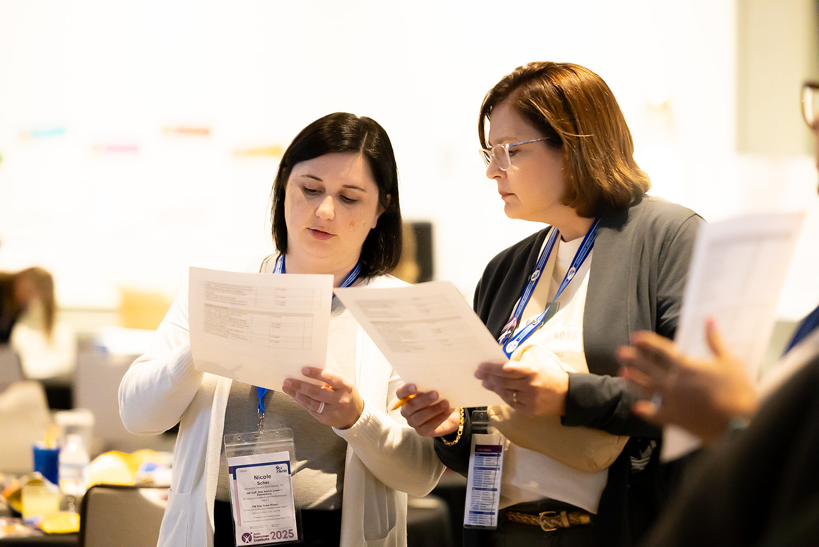 Two individuals reading documents at an event or conference, wearing lanyards with name tags.