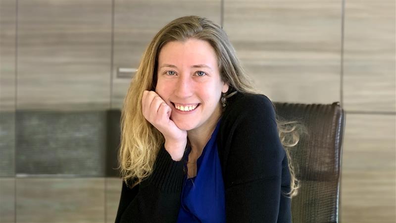 Person with long hair sitting in a chair, partially covering their face with their hand; blurred face.
