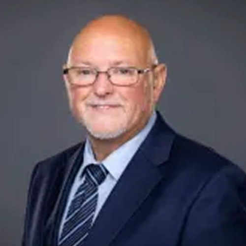 An individual wearing a formal suit and tie against a plain background. The face has been pixelated for privacy.