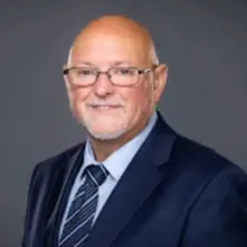 An individual wearing a formal suit and tie against a plain background. The face has been pixelated for privacy. An individual wearing a formal suit and tie against a plain background. The face has been pixelated for privacy.