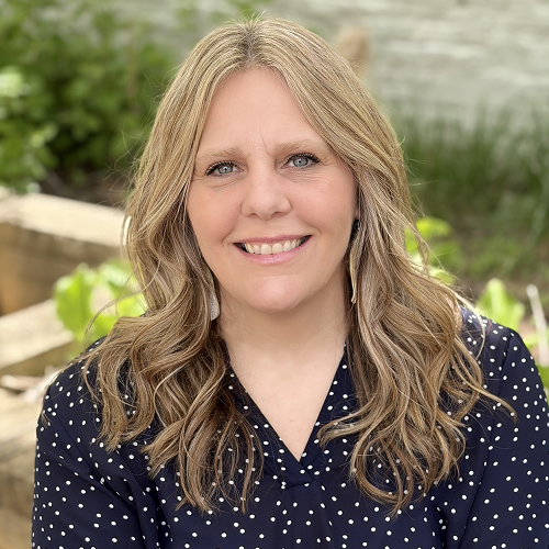 A portrait of an individual with long, wavy hair wearing a polka dot shirt in an outdoor setting.