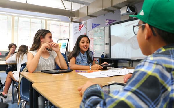 A classroom scene with students sitting at desks and using tablets. A classroom scene with students sitting at desks and using tablets.