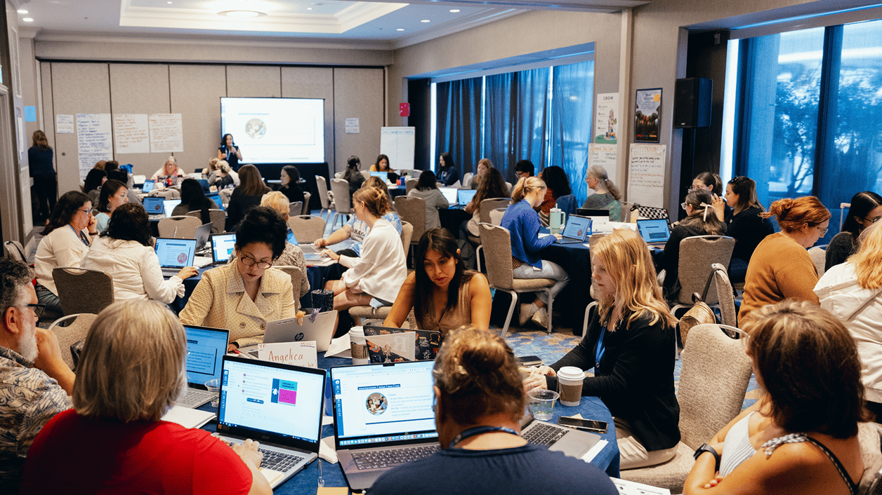 A group of people participating in a workshop or conference, sitting at tables with laptops in a meeting room. A group of people participating in a workshop or conference, sitting at tables with laptops in a meeting room.