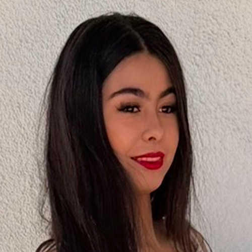 Person with long dark hair standing against a textured wall.