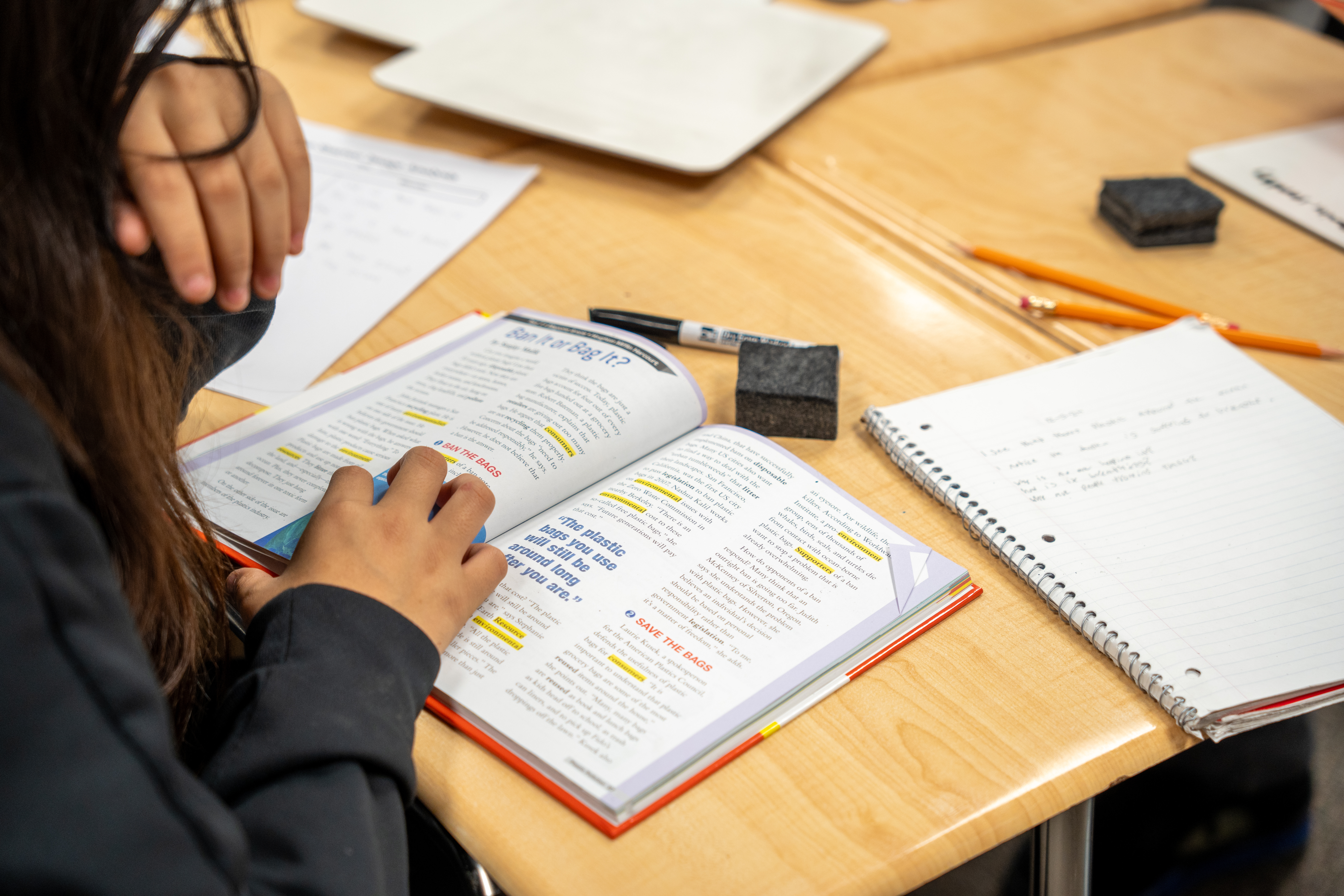 Person reading an open book at a desk with a notebook, pencils, and other study materials.