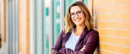 Person leaning against a brick wall with crossed arms wearing a purple jacket and white shirt. Person leaning against a brick wall with crossed arms wearing a purple jacket and white shirt.
