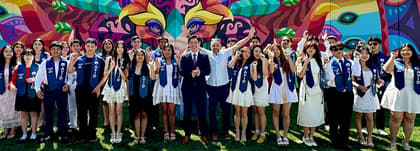 A large group of people wearing graduation stoles, posing in front of a colorful mural. A large group of people wearing graduation stoles, posing in front of a colorful mural.