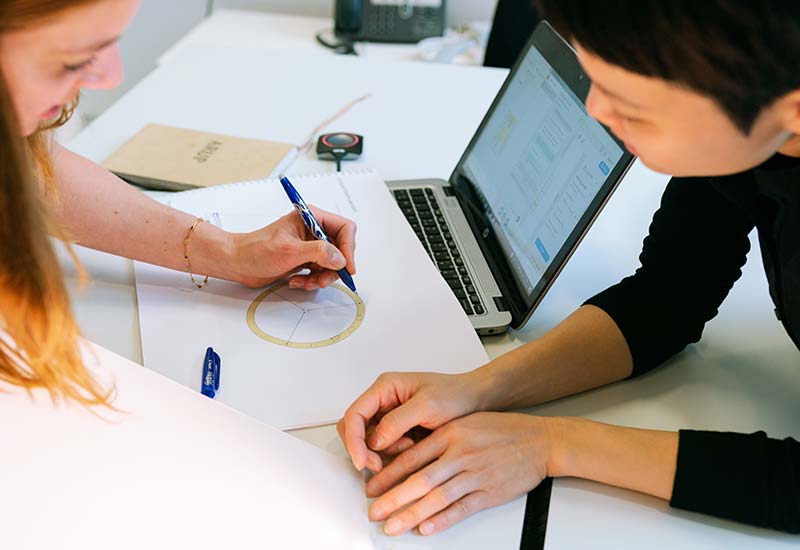 Two individuals collaborating with a laptop and notes on a desk.
