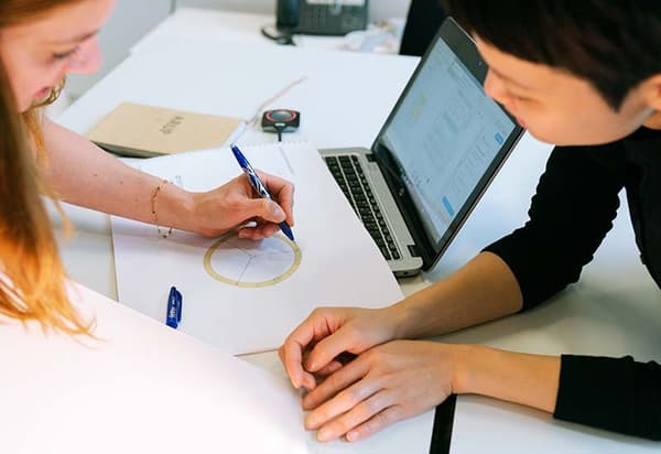 Two individuals collaborating with a laptop and notes on a desk. Two individuals collaborating with a laptop and notes on a desk.