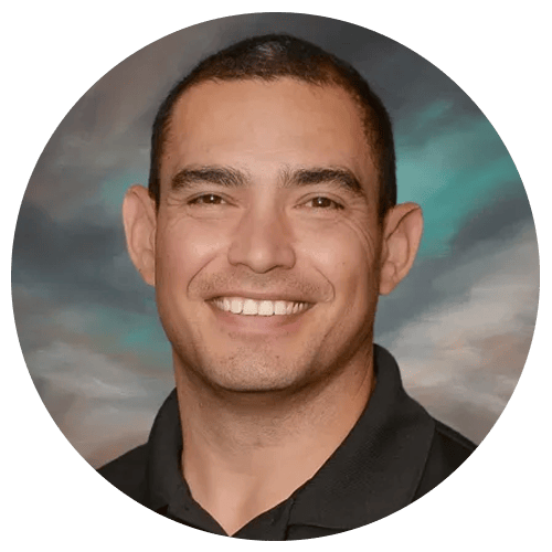 A person wearing a black collared shirt, set against a background with green and grey hues. A person wearing a black collared shirt, set against a background with green and grey hues.