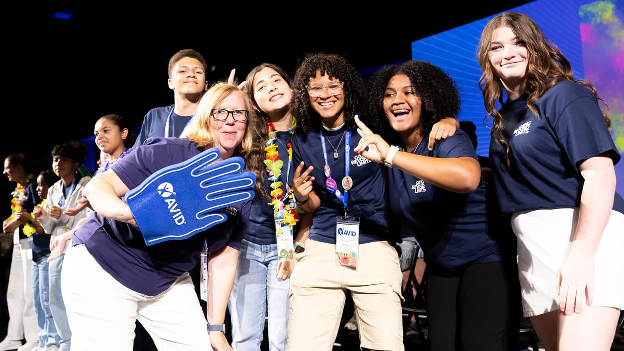 Group of people wearing AVID shirts and lanyards, some holding up signs, posing together. Group of people wearing AVID shirts and lanyards, some holding up signs, posing together.