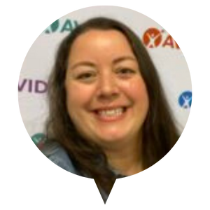 Individual with long, dark hair standing in front of a white backdrop featuring various logos.