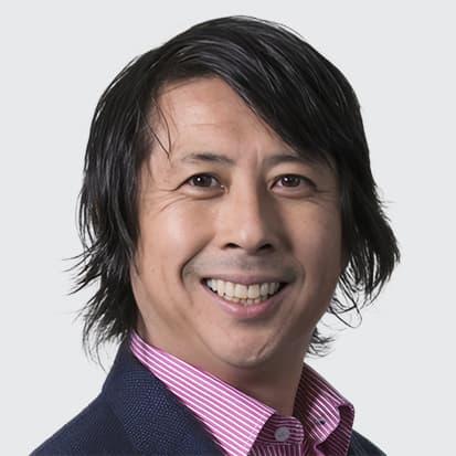 Individual with medium-length dark hair wearing a dark jacket over a pink and white striped collared shirt. Individual with medium-length dark hair wearing a dark jacket over a pink and white striped collared shirt.