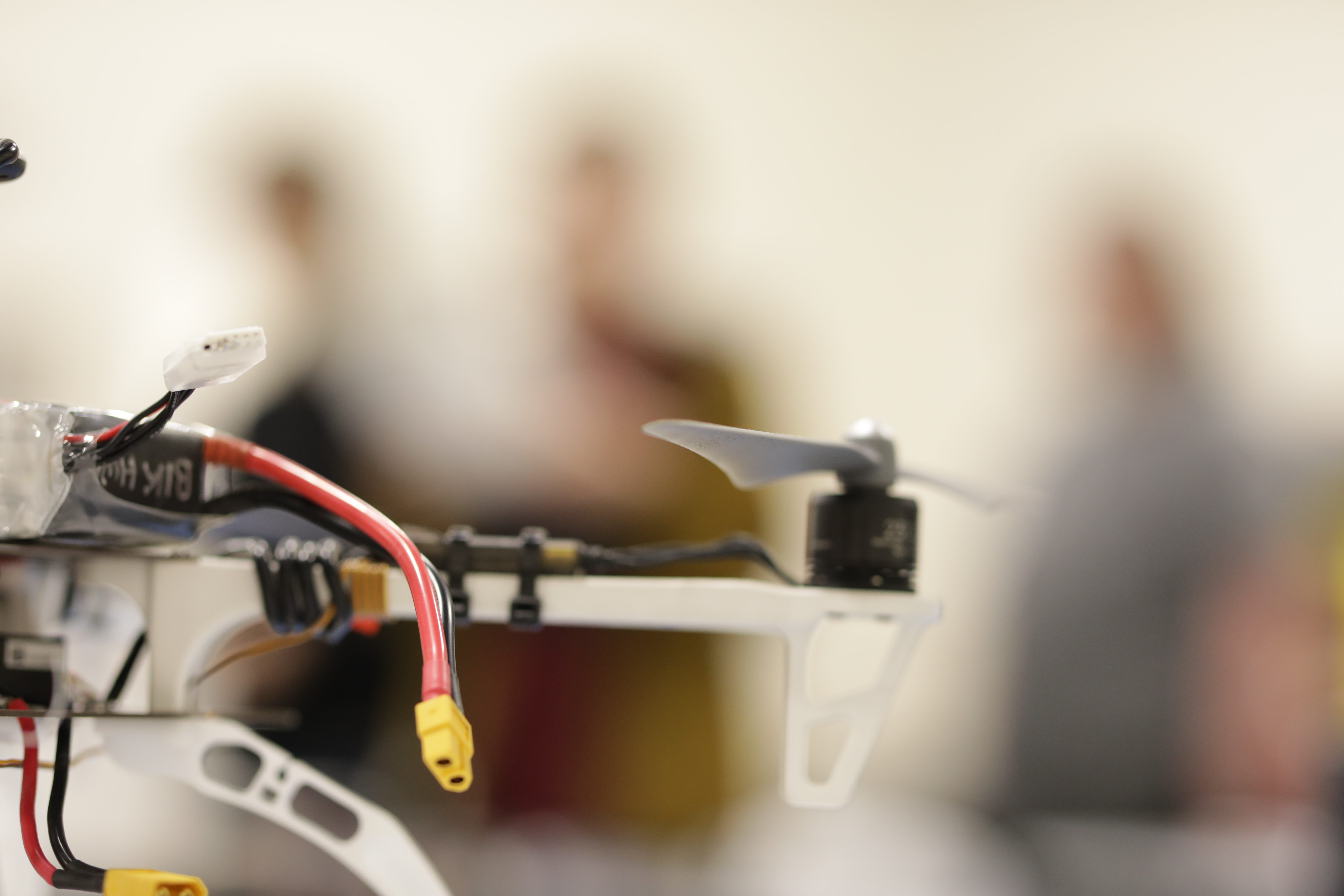 Close-up view of a drone with visible wires and a propeller, with blurred background.