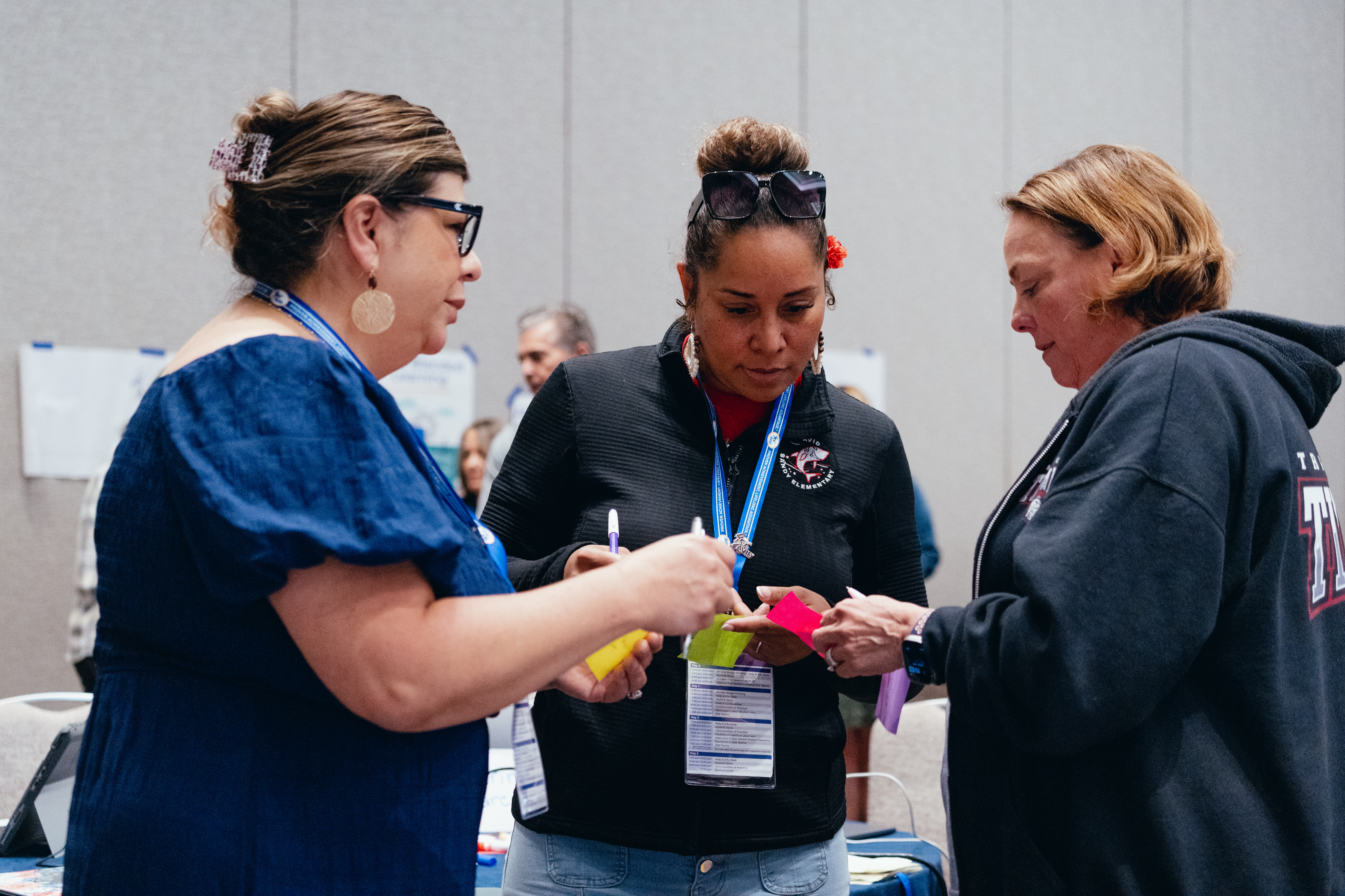 Three people are interacting at an event, holding papers and wearing event badges in a conference setting.