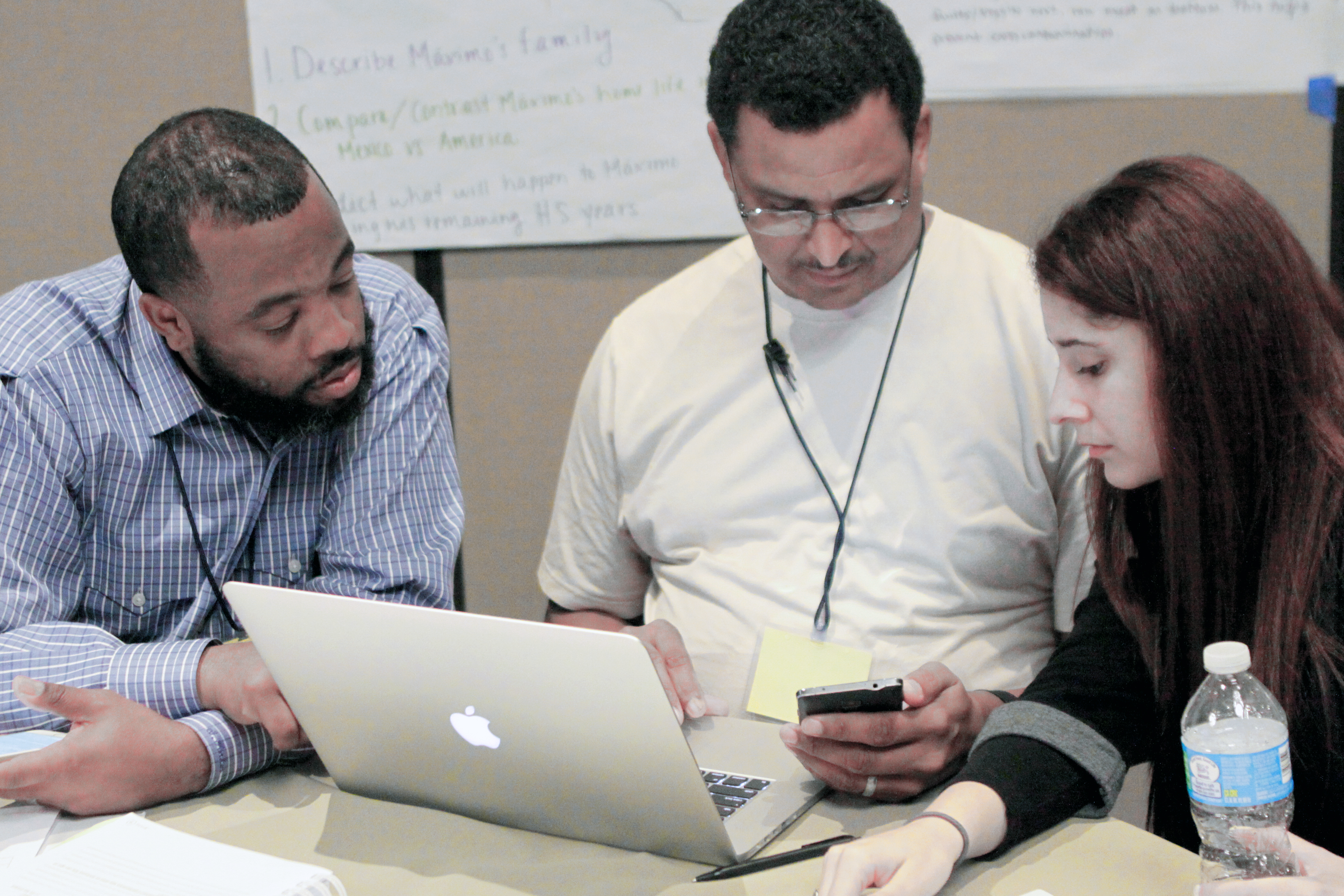 Three people collaborating at a table with a laptop and smartphone.