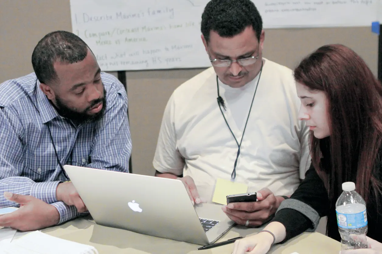 Three people collaborating at a table with a laptop and smartphone. Three people collaborating at a table with a laptop and smartphone.
