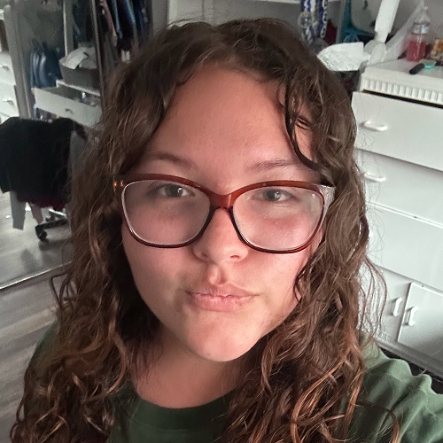 Image of a person with curly hair in a room with a reflection visible in the background mirror.