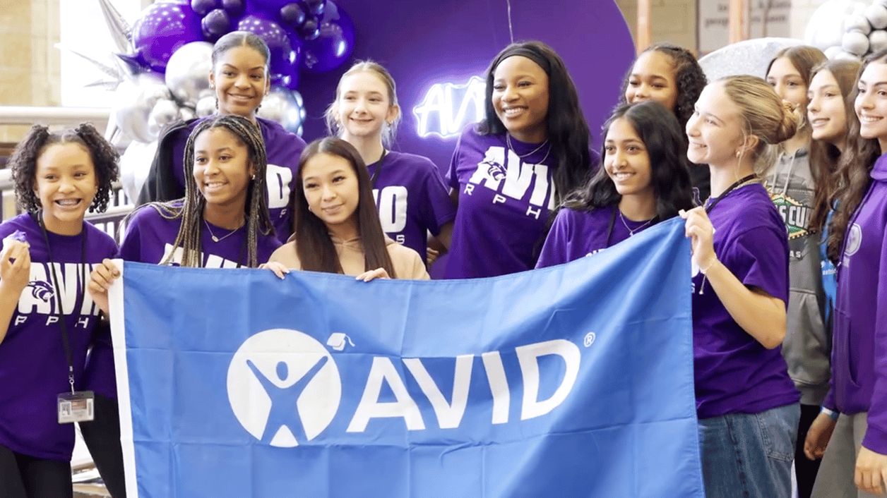 Group of individuals holding an AVID banner with a balloon arrangement in the background. Group of individuals holding an AVID banner with a balloon arrangement in the background.