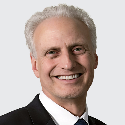 A person with short gray hair wearing a suit and tie against a plain background.