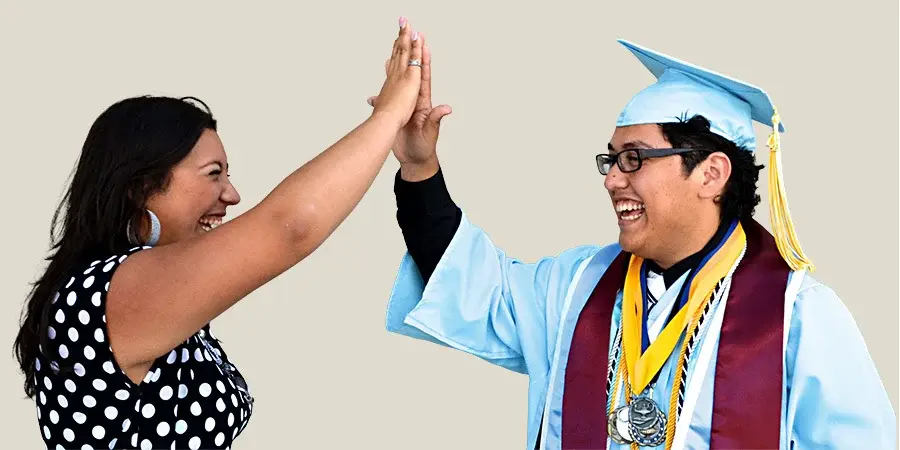 Two people giving high fives, with one dressed in graduation attire.