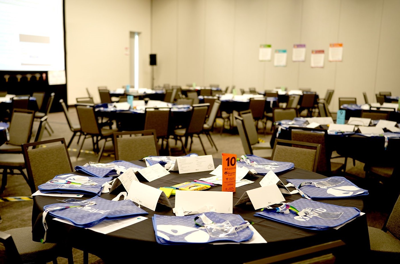 A conference room with tables set up, covered in blue-tote welcome materials and name cards.