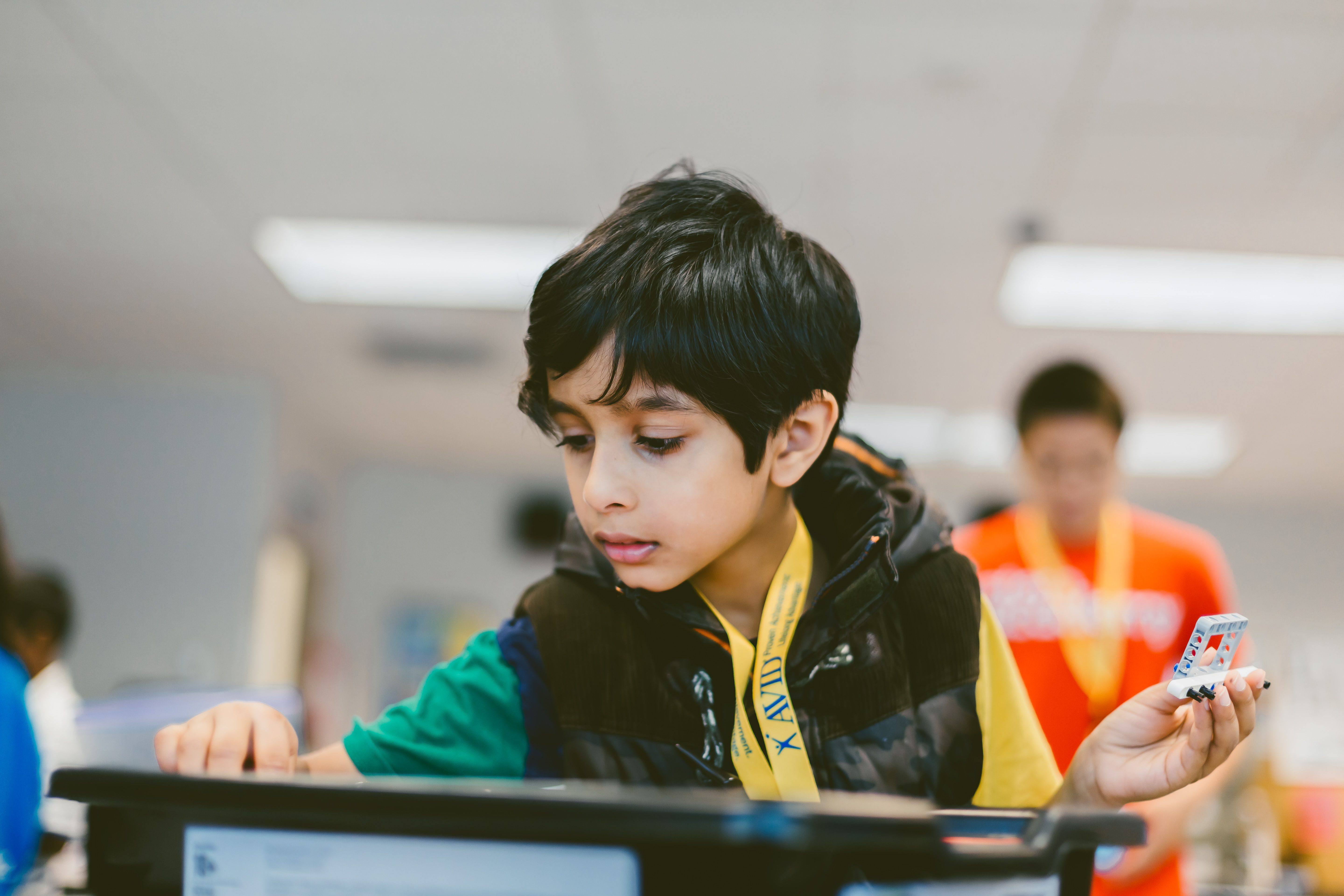 A person in a green and yellow shirt working with an electronic device on a workbench in a classroom setting.