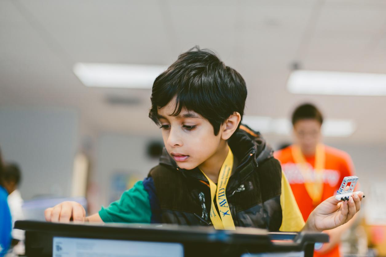 A person in a green and yellow shirt working with an electronic device on a workbench in a classroom setting. A person in a green and yellow shirt working with an electronic device on a workbench in a classroom setting.