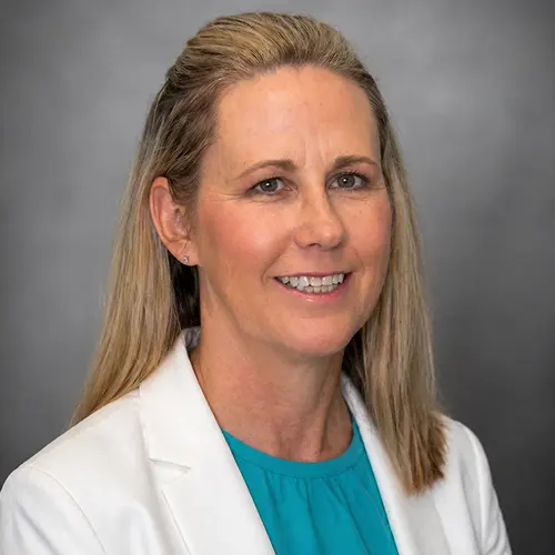Portrait of individual with blurred face, wearing a white blazer and teal shirt, against a gray background. Portrait of individual with blurred face, wearing a white blazer and teal shirt, against a gray background.