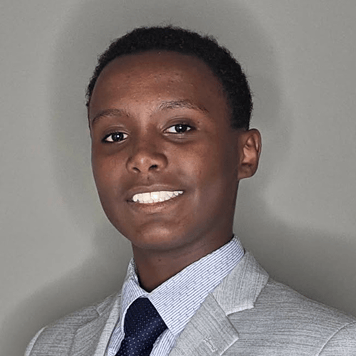 Individual wearing a light gray suit jacket, light blue dress shirt, and dark tie. Individual wearing a light gray suit jacket, light blue dress shirt, and dark tie.