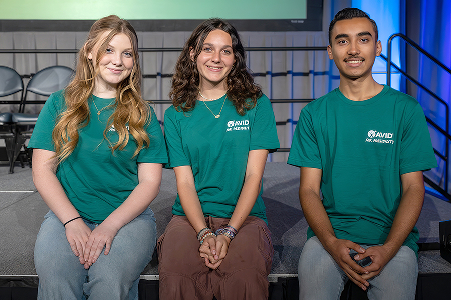 Three people sitting side by side wearing green shirts, posing for a photo.