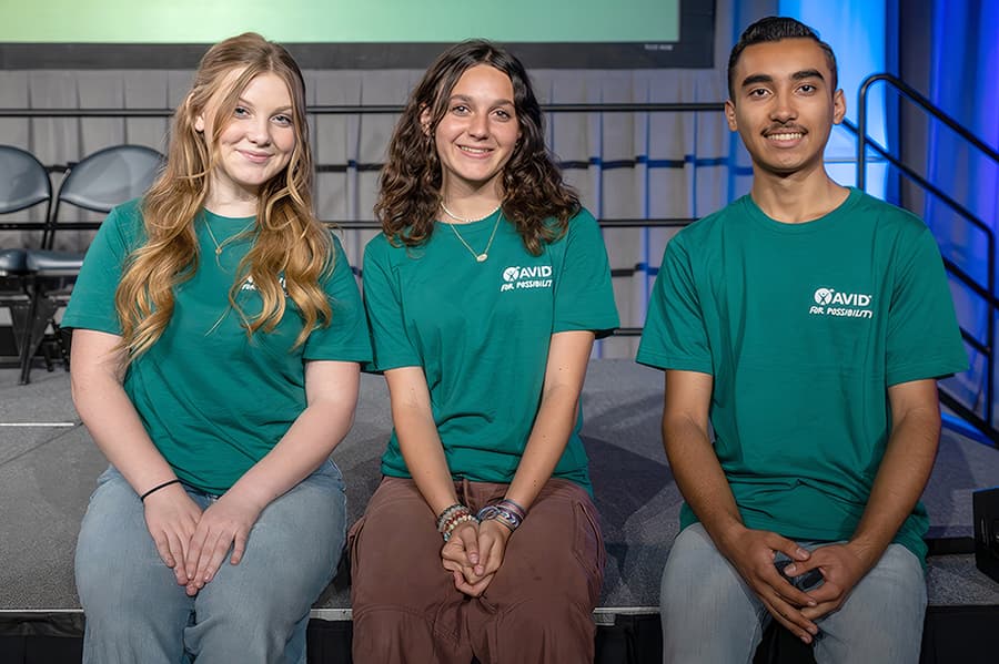 Three people sitting side by side wearing green shirts, posing for a photo. Three people sitting side by side wearing green shirts, posing for a photo.