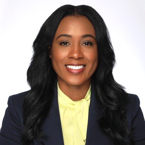 Person with long dark hair wearing a blue blazer and a yellow shirt.