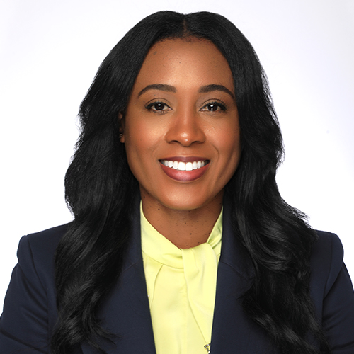 Person with long dark hair wearing a blue blazer and a yellow shirt.