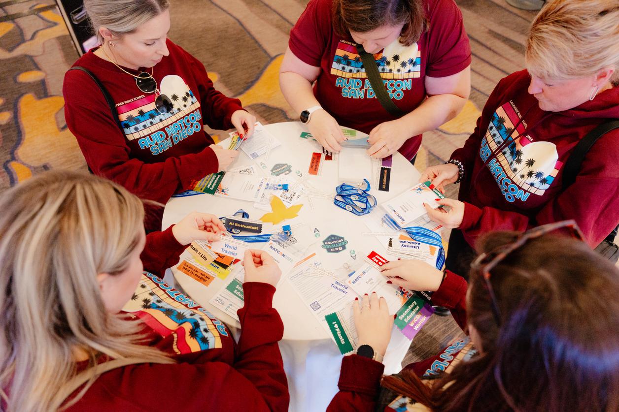 A group of individuals seated around a table examining name badges at a convention. A group of individuals seated around a table examining name badges at a convention.