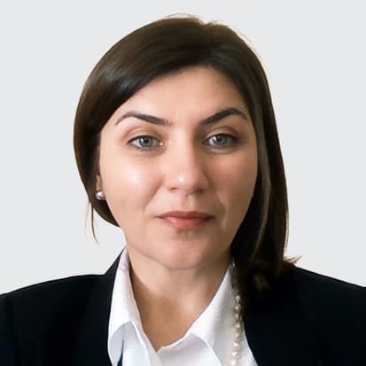 A person with shoulder-length brown hair wearing a black blazer, white shirt, and pearl necklace. A person with shoulder-length brown hair wearing a black blazer, white shirt, and pearl necklace.