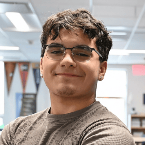 Person standing indoors with blurred face, wearing a patterned long-sleeve shirt. Office or classroom background. Person standing indoors with blurred face, wearing a patterned long-sleeve shirt. Office or classroom background.