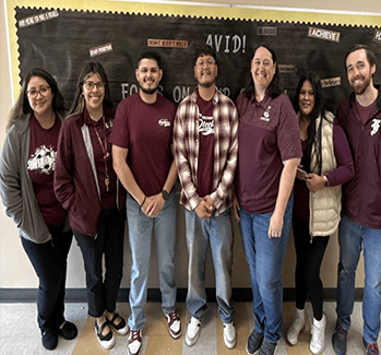 Group photo of seven people standing in front of a blackboard. They are wearing casual outfits, mostly in maroon and white tones. Group photo of seven people standing in front of a blackboard. They are wearing casual outfits, mostly in maroon and white tones.
