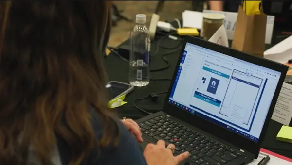 A person working on a laptop at a desk with several items including a phone, water bottle, and papers. A person working on a laptop at a desk with several items including a phone, water bottle, and papers.