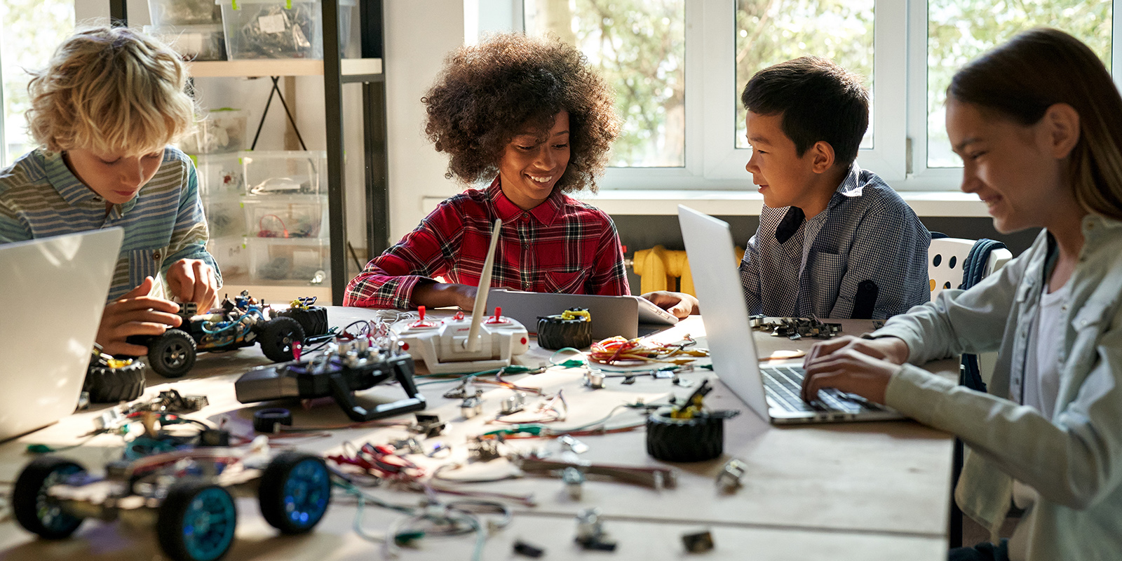 A group of people working on robotics and laptops at a table in a well-lit room.