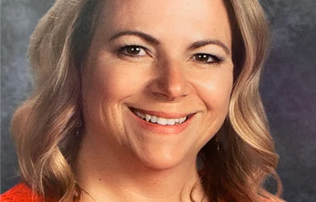 Individual with shoulder-length wavy hair wearing a red top, grayish background